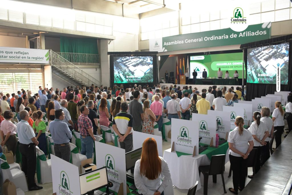 Grupo de personas de pie en gran reunión de asamblea en amplio coliseo con pantallas grandes