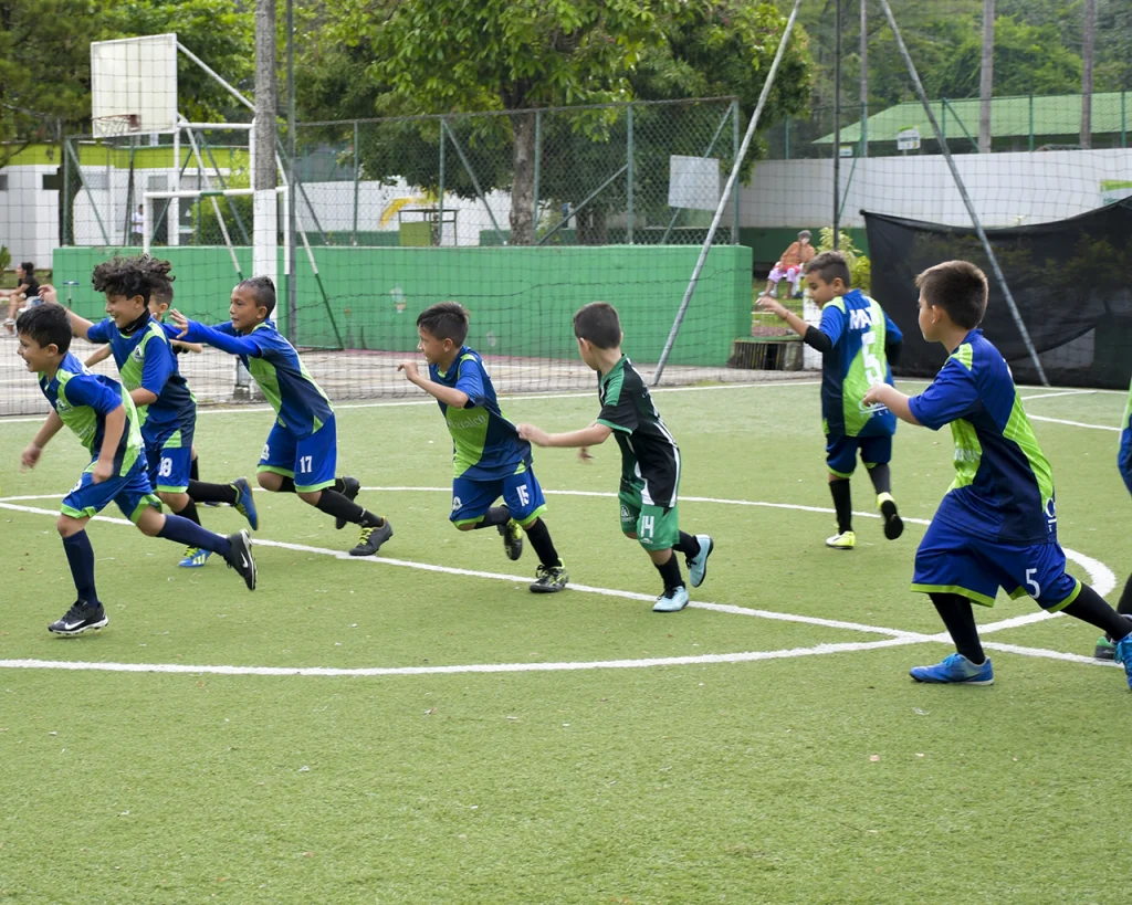 Grupo de niños con uniforme corriendo en cancha de fútbol