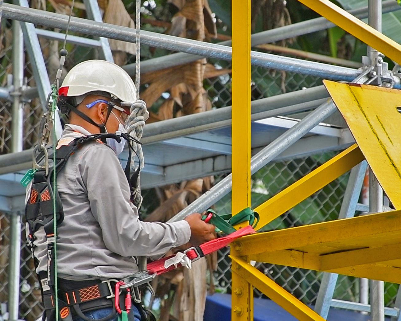 Hombre trabajando en alturas con casco blanco enganchando cuerda