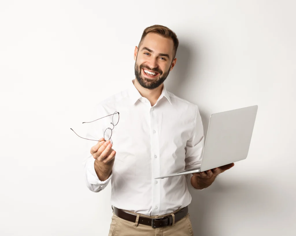 Hombre sonriendo con lentes en su mano derecha y computador portátil en su mano izquierda