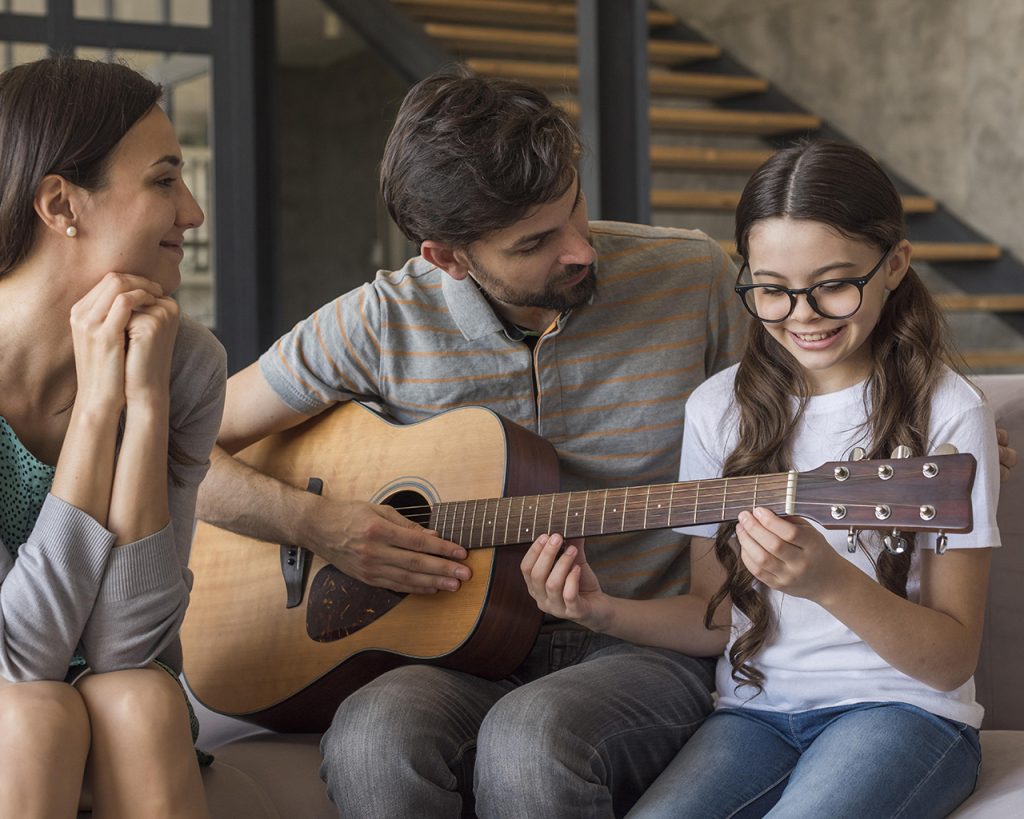 Mujer, padre e hija aprendiendo a tocar la guitarra acústica