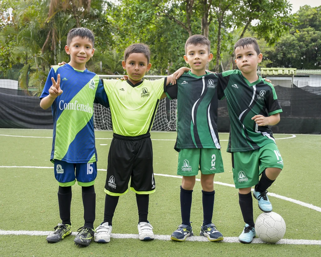 Grupo de niños con uniforme y balón de fútbol abrazados y saludando