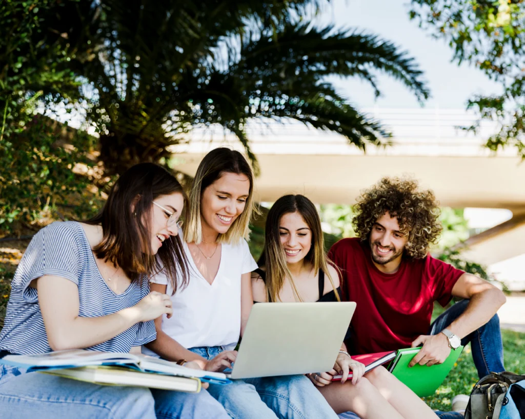 Cuatro jóvenes estudiantes alegres viendo computadora portatil