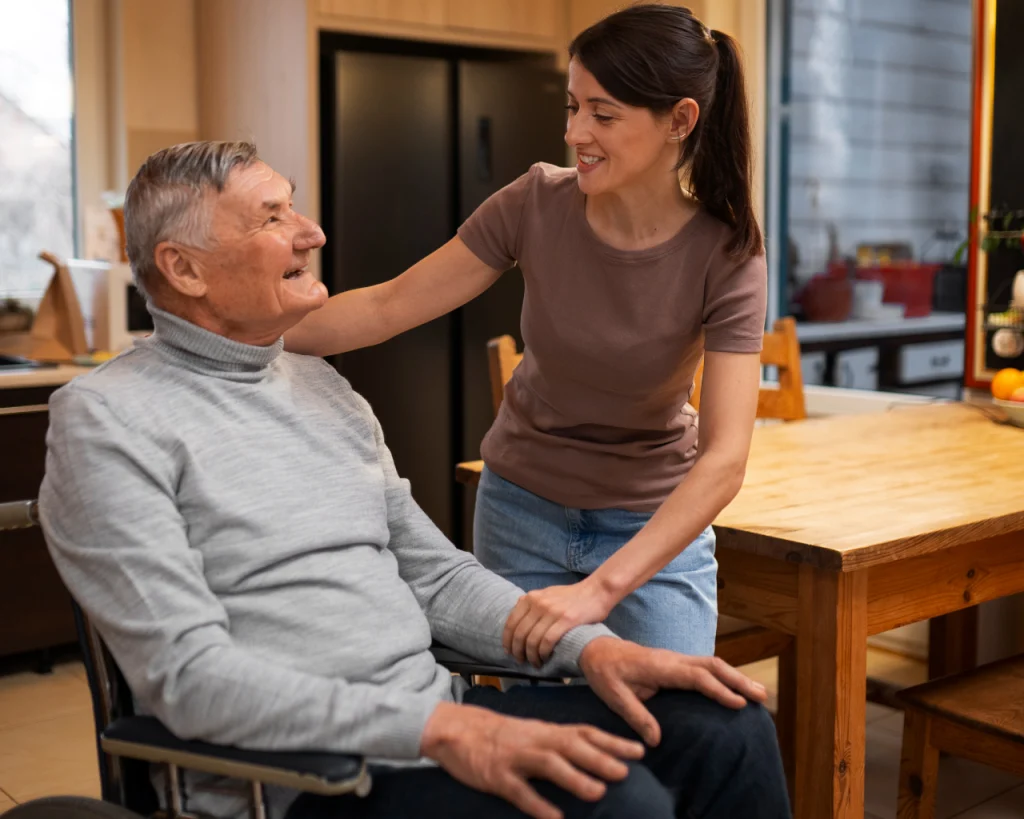 Mujer conversando con hombre de la tercera edad en silla de ruedas en la cocina de la casa