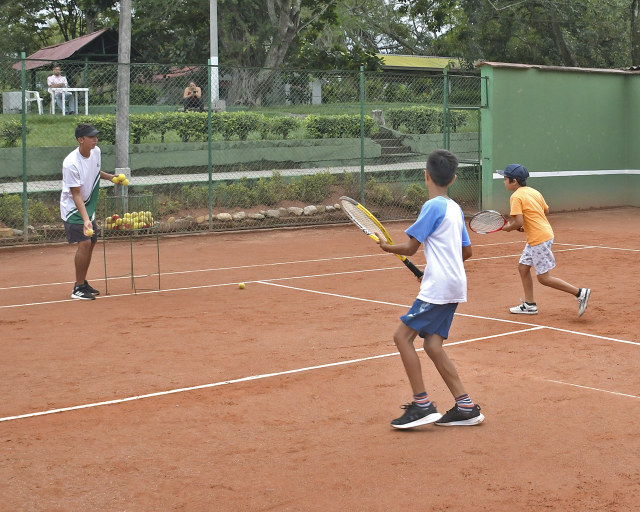 Instructor deportivo lanzando pelotas de tenis a niños que entrenan en la cancha con sus raquetas