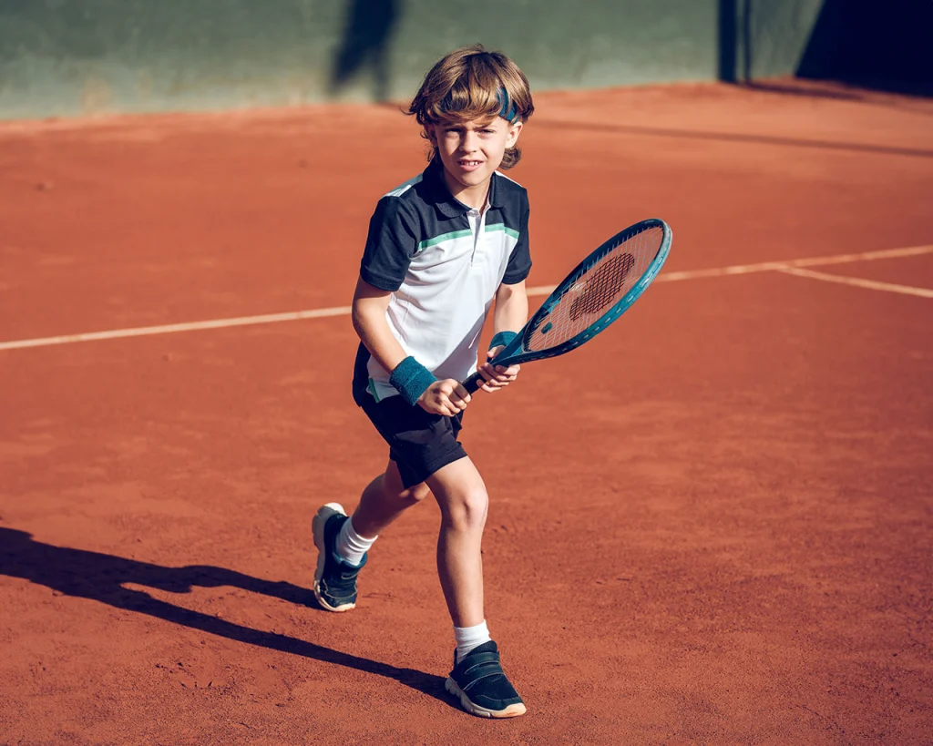 Niño en cancha de tenis de campo con uniforme y raqueta